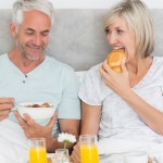 Happy mature couple having breakfast in bed at home
