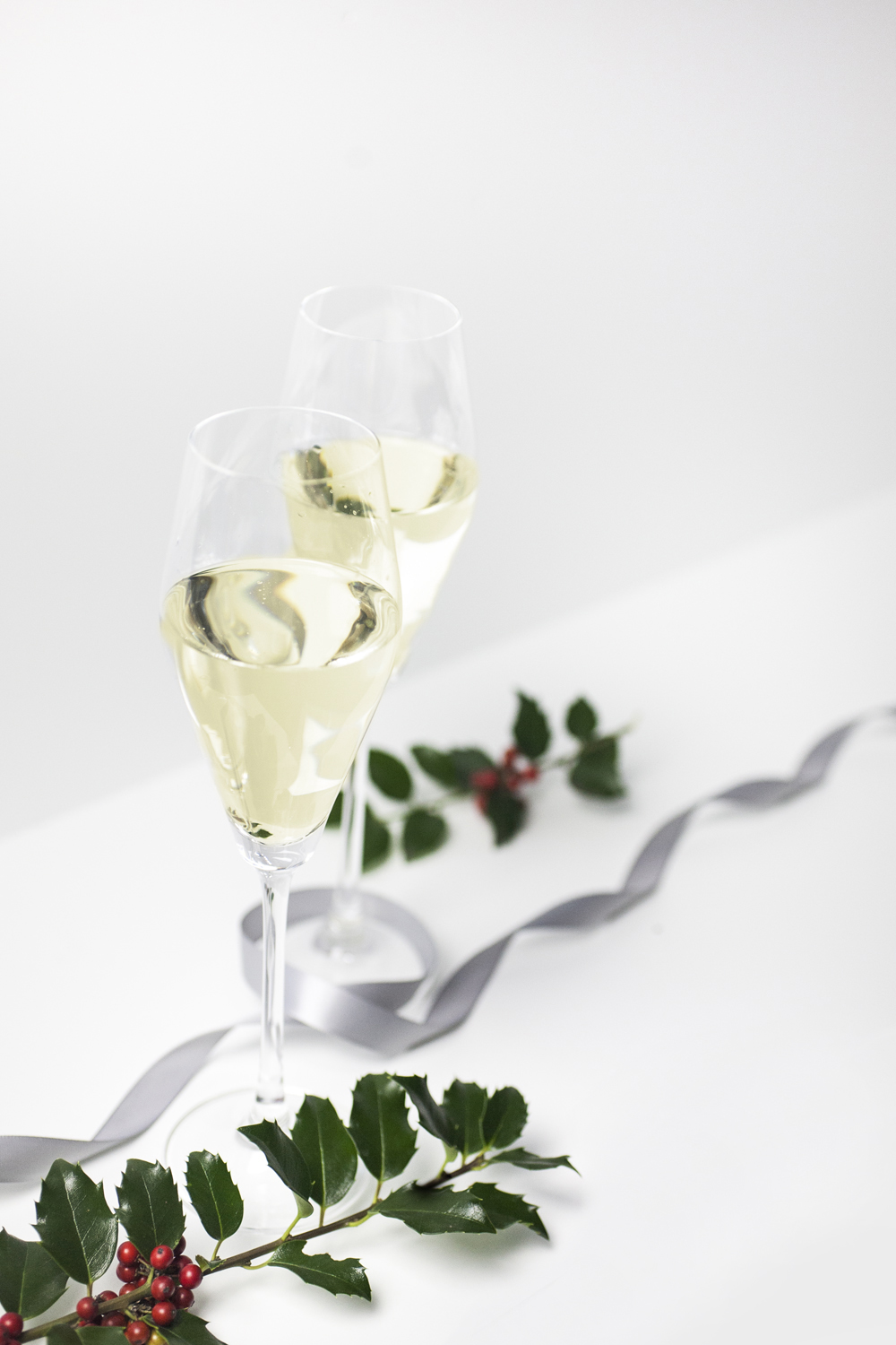two champagne flutes with holly and ribbons